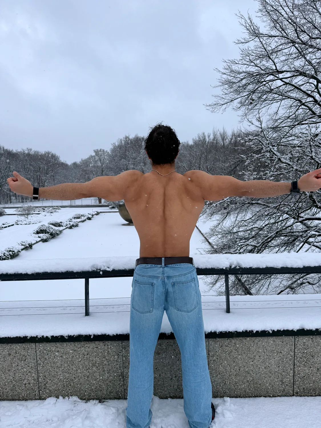Rückenansicht mit ausgebreiteten Armen über einem verschneiten Kanal in Berlin.